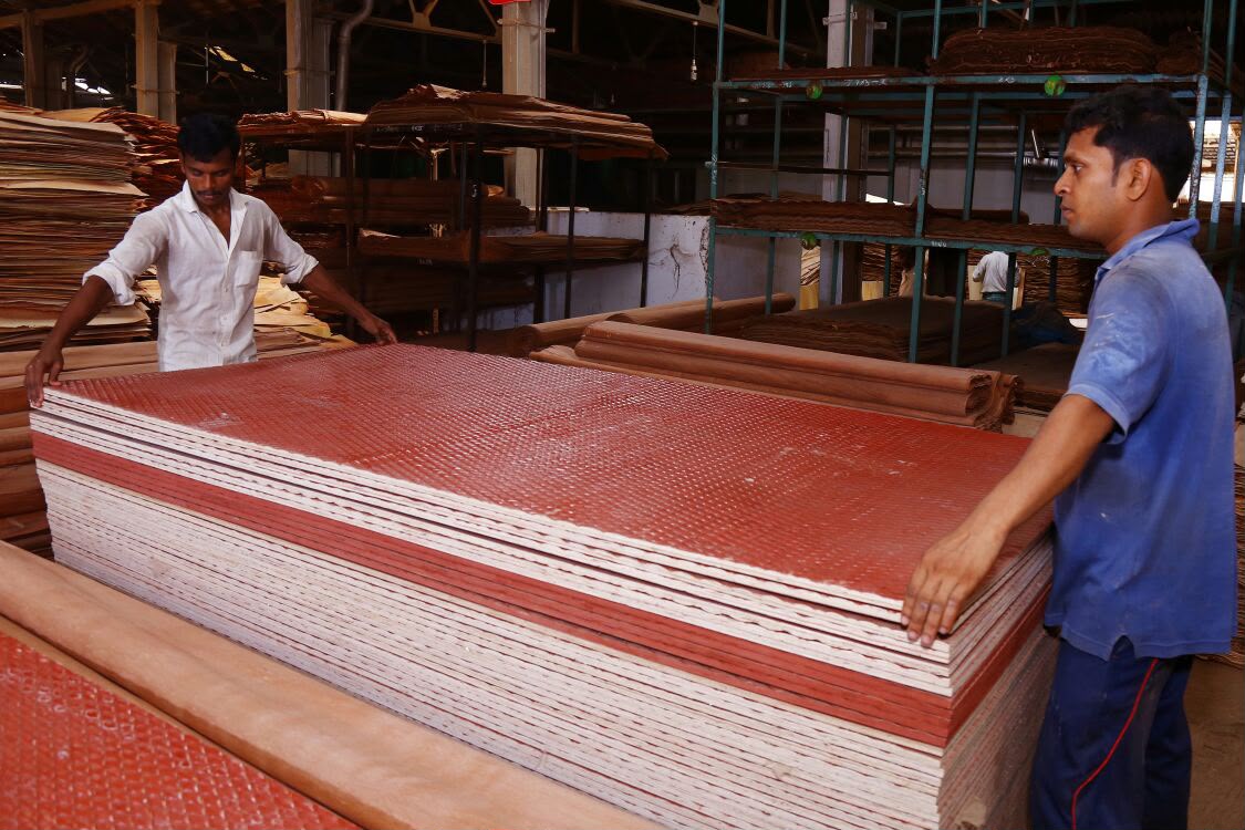 Workers handling stacked film-faced plywood panels on the factory floor